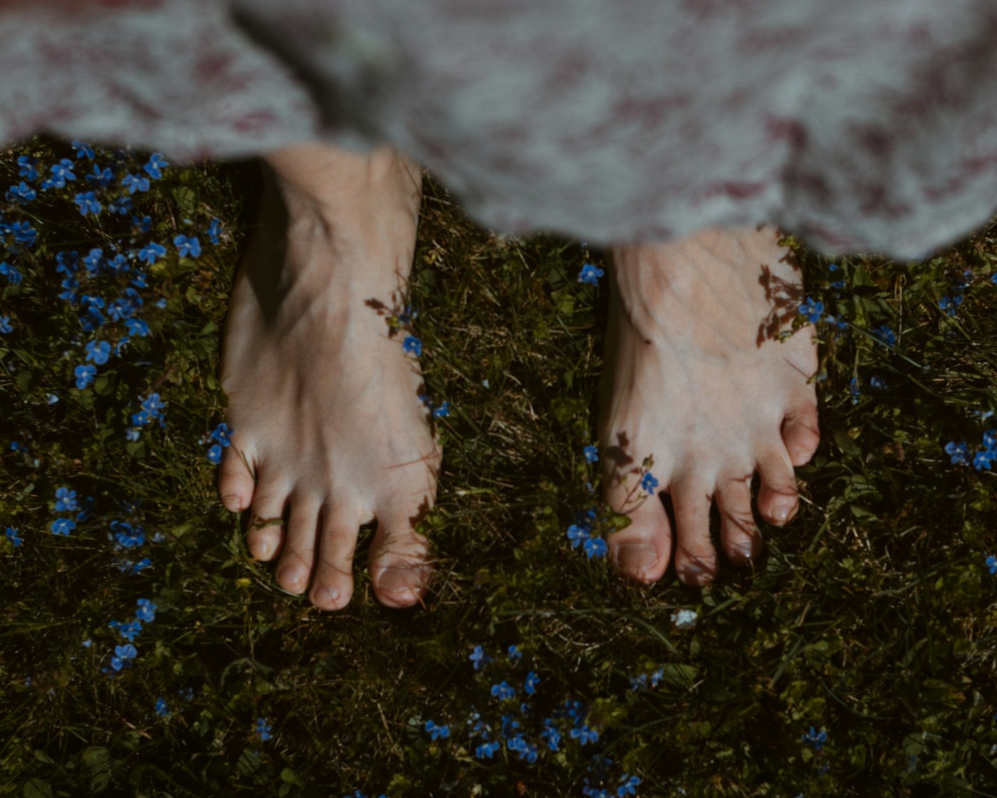 Pies descalzos sobre el pasto con pequeñas flores azules
